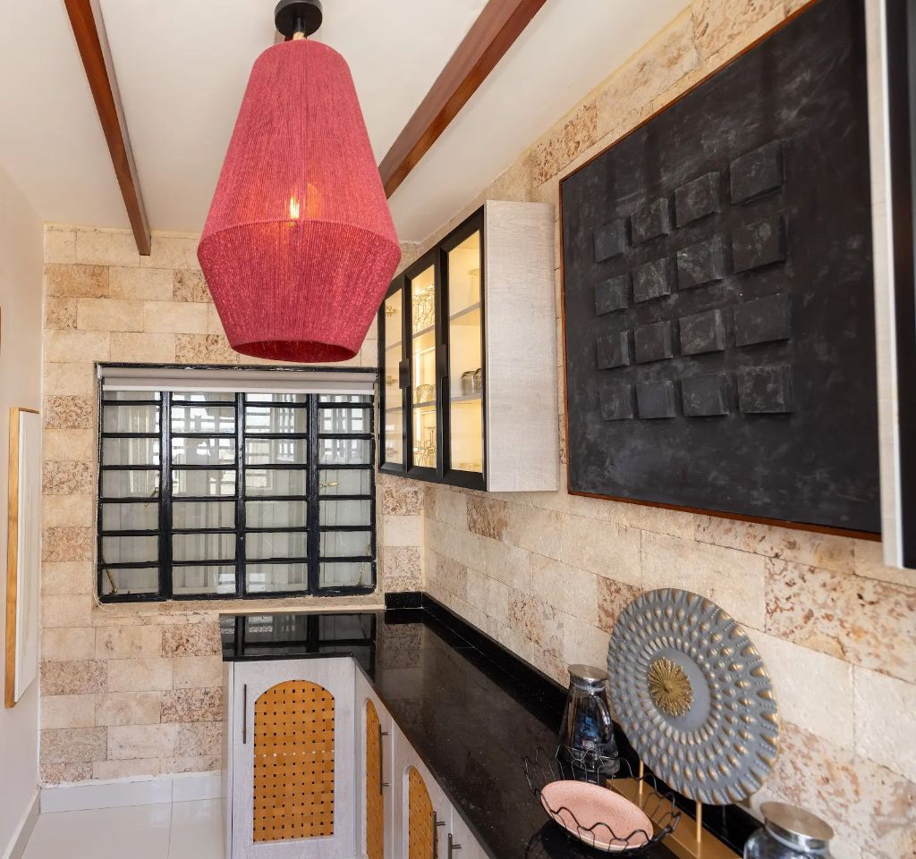 Stone-clad servery kitchen with red pendant light and glass display cabinetry