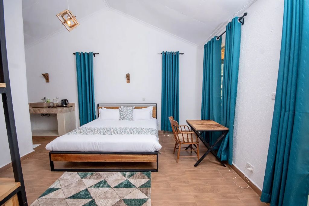 Teal-curtained boutique hotel bedroom with wood-frame bed and vaulted ceiling