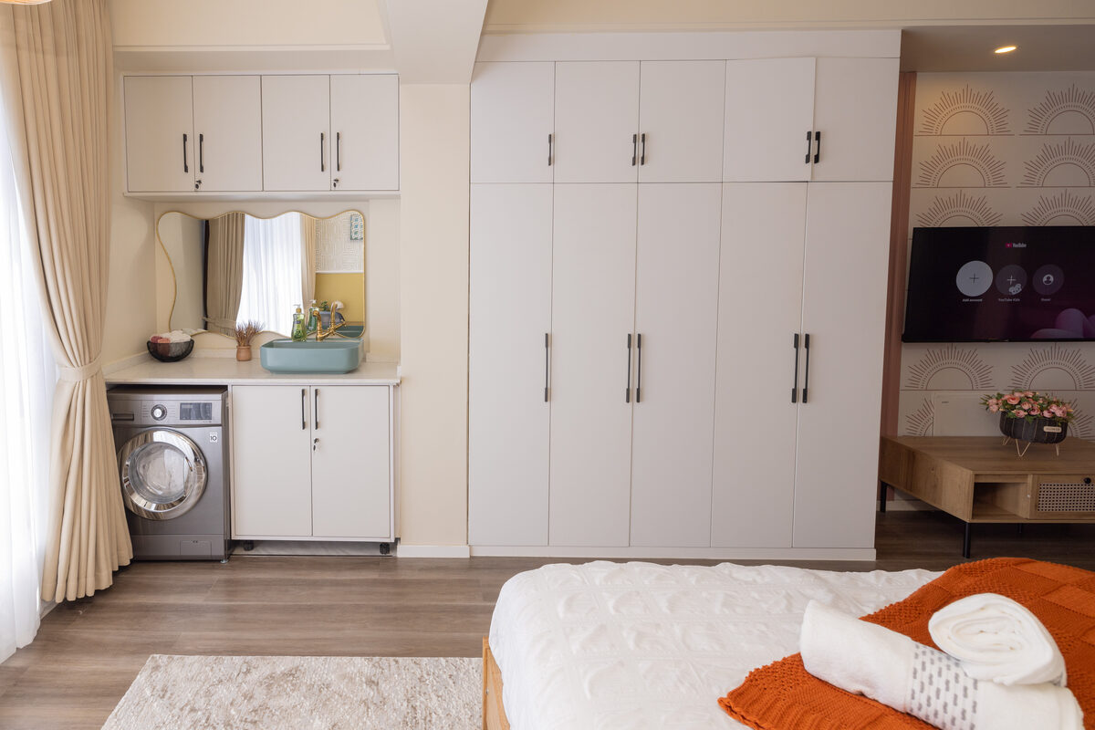 After: laundry nook with white cabinetry, scalloped mirror, teal vessel sink, gold faucet and front-load washer beside built-in wardrobes
