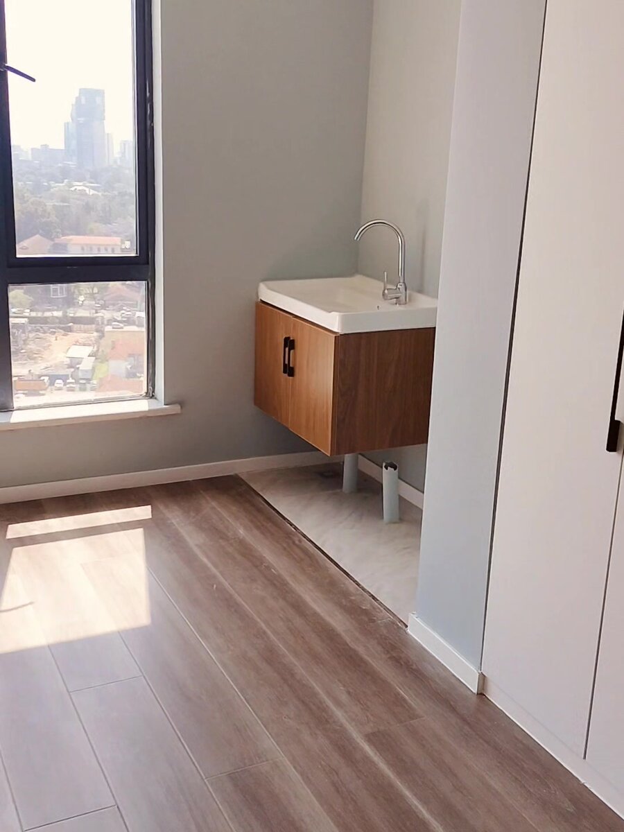 Before: empty studio corner with bare plumbing stub, no cabinetry and unfinished walls