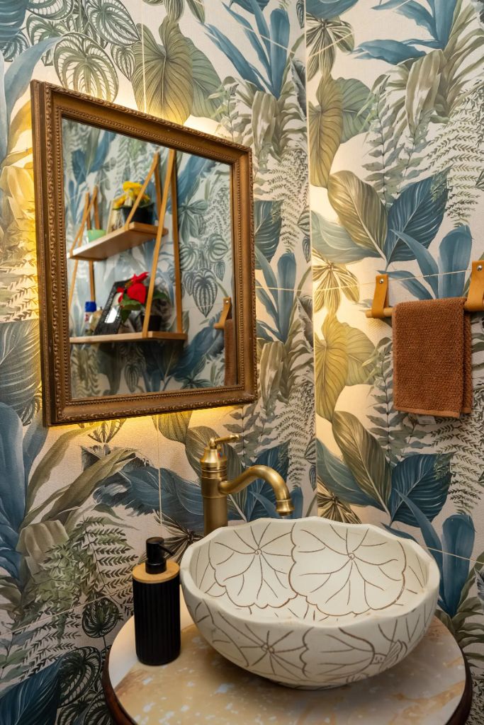 Botanical wallpaper powder room with carved vessel sink and gold-framed mirror