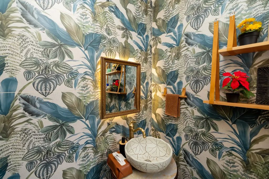 Carved vessel sink with brass tap against botanical wallpaper